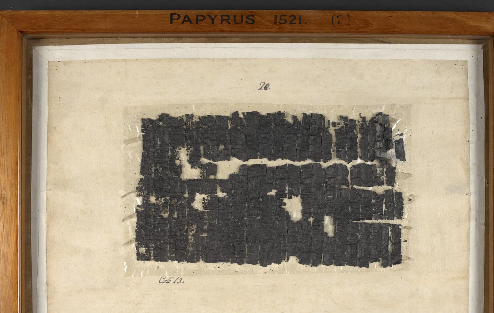 A carbonised Herculaneum papyrus, unrolled and mounted in a wooden display frame labelled Papyrus 1521